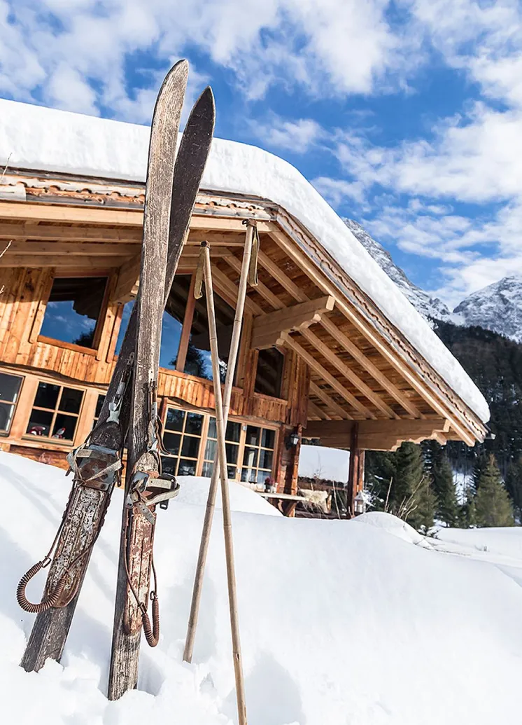 Vintage-Ski und -Stöcke im tiefen Schnee vor traditionellem Tiroler Holzchalet