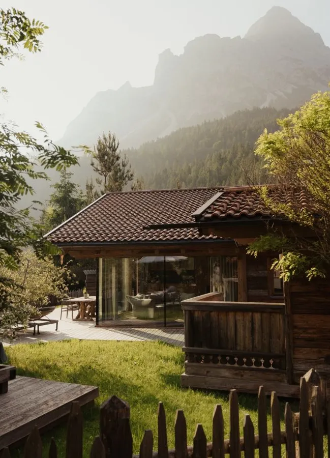 Holzchalet mit Glasfronttüren und Terrasse bei sommerlichem Bergblick durch Fichtenrahmen