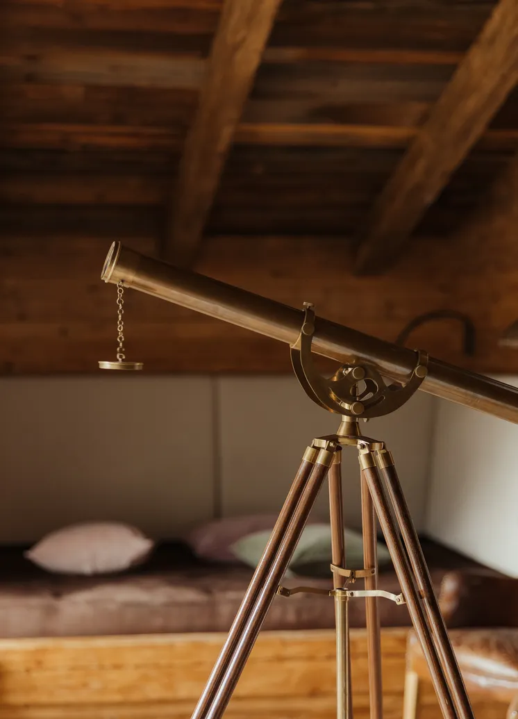 Vintage-Messingteleskop auf Holzstativ im rustikalen Chalet mit Altholzbalken und Ledersessel