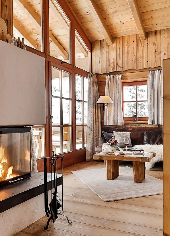 Chalet-Wohnzimmer mit dreiteiligem Kamin, Holzbalken, Ledersofa und Sheepskin-Wurfdecken
