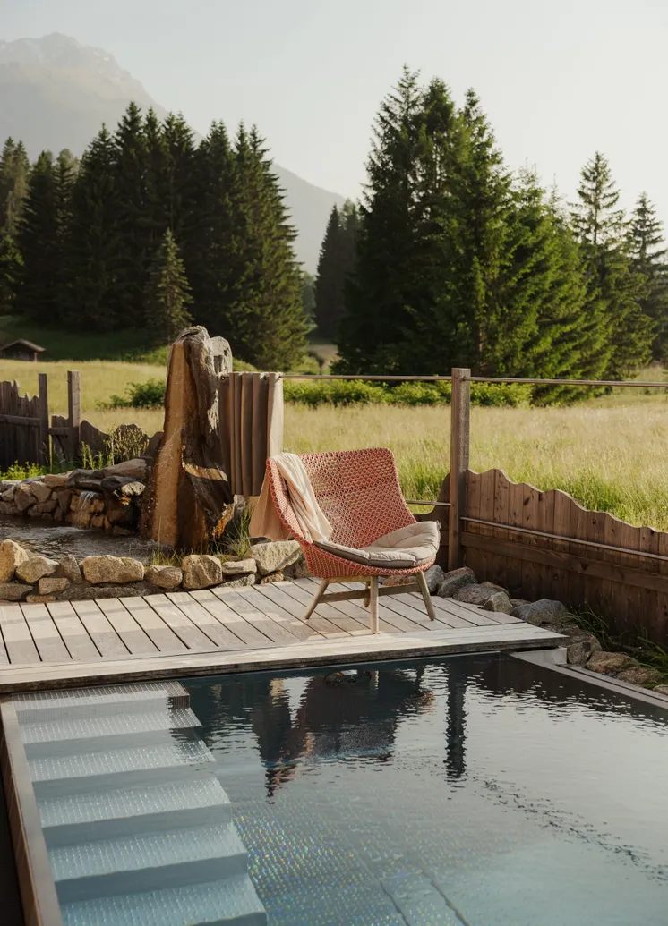 Pool-Deck mit korallfarbigem Liegestuhl, Naturstein-Holzdetails und Bergwiesen-Panorama