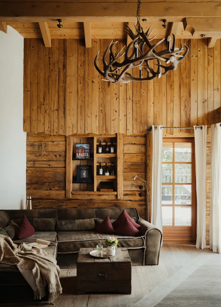 Hochwandiger Chalet-Wohnraum mit Altholzwänden, Geweih-Kronleuchter und Ledersofa