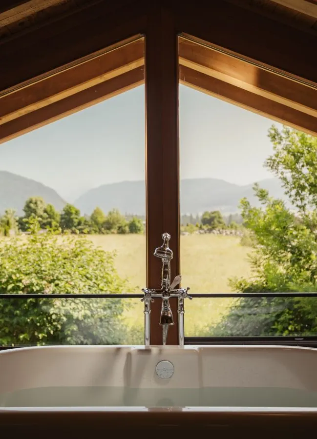 Freistehende weiße Badewanne unter Giebelfenster mit Blick auf Tiroler Sommerlandschaft