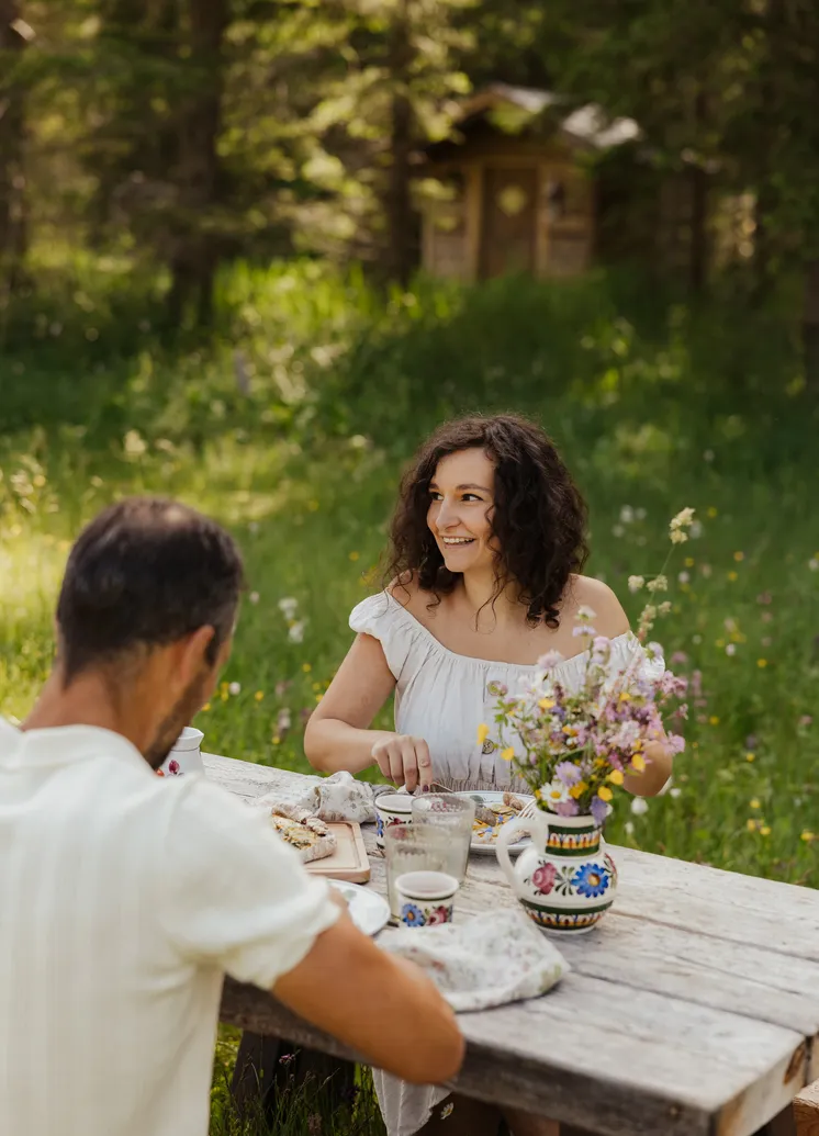 Lachendes Paar beim romantischen Abendessen am rustikalen Holztisch in der Almwiese