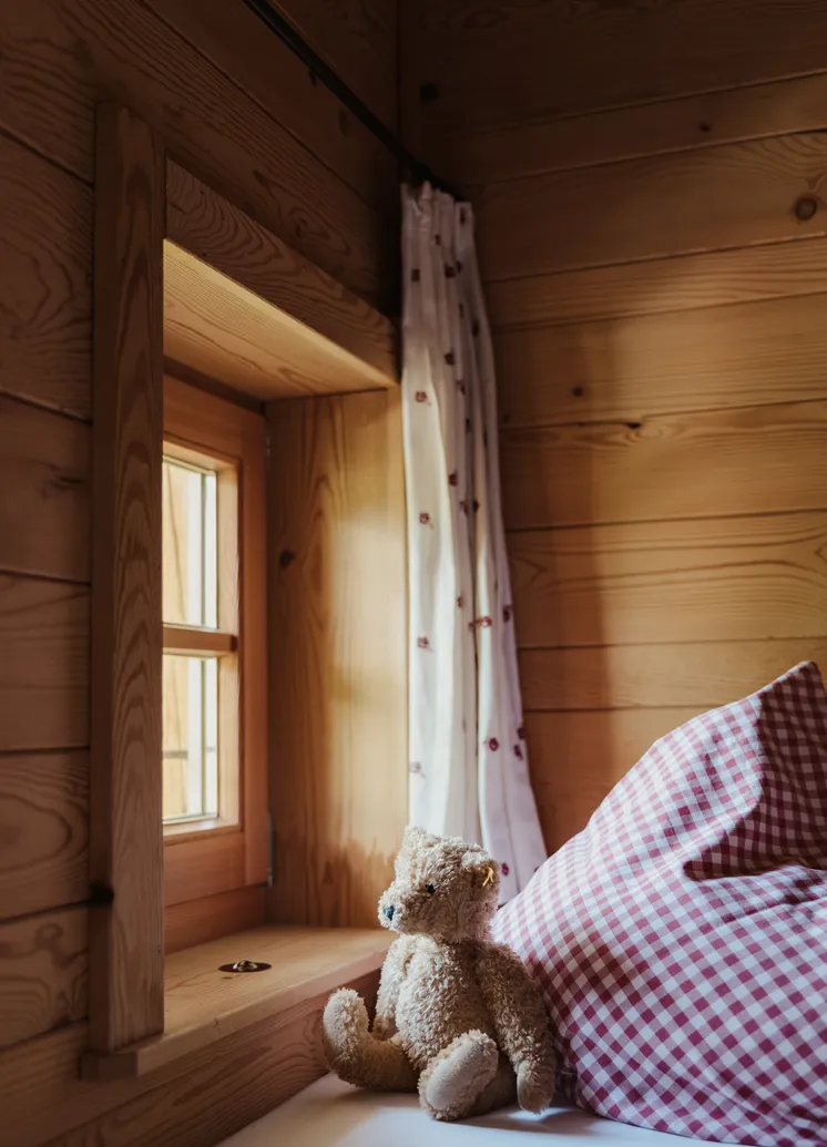Gemütliche Kindernische in einem Holzchalet mit Teddybär und karierten Kissen