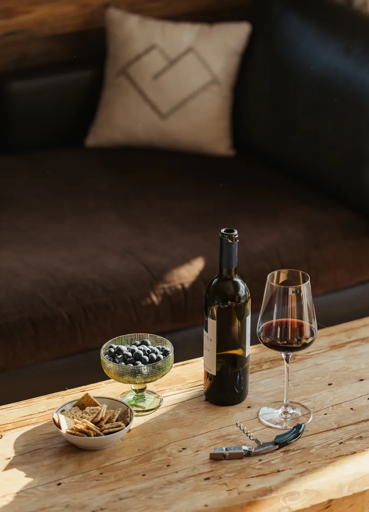 Weinflasche, Rotweinglas und Blaubeeren auf Holztisch vor Ledersofa mit LaPosch-Kissen